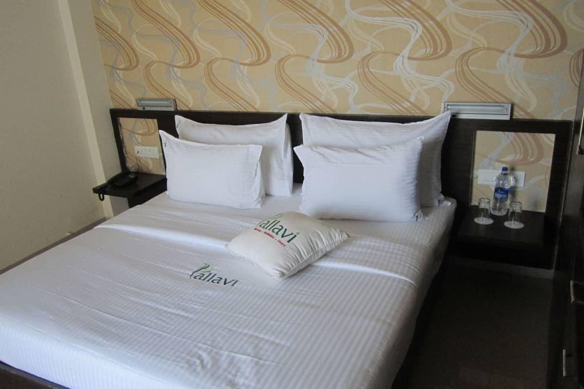 A neatly made bed with white linens and pillows, a bedside table with a bottle and glasses, and a patterned wall in the background.