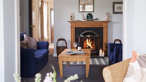 Una sala de estar acogedora con chimenea, sofás azules, una mesa de centro de madera y una puerta que da a otra habitación.