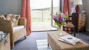 Una habitación con un sofá de mimbre, una pequeña mesa con un jarrón de flores, una silla de madera y un aparador con libros.