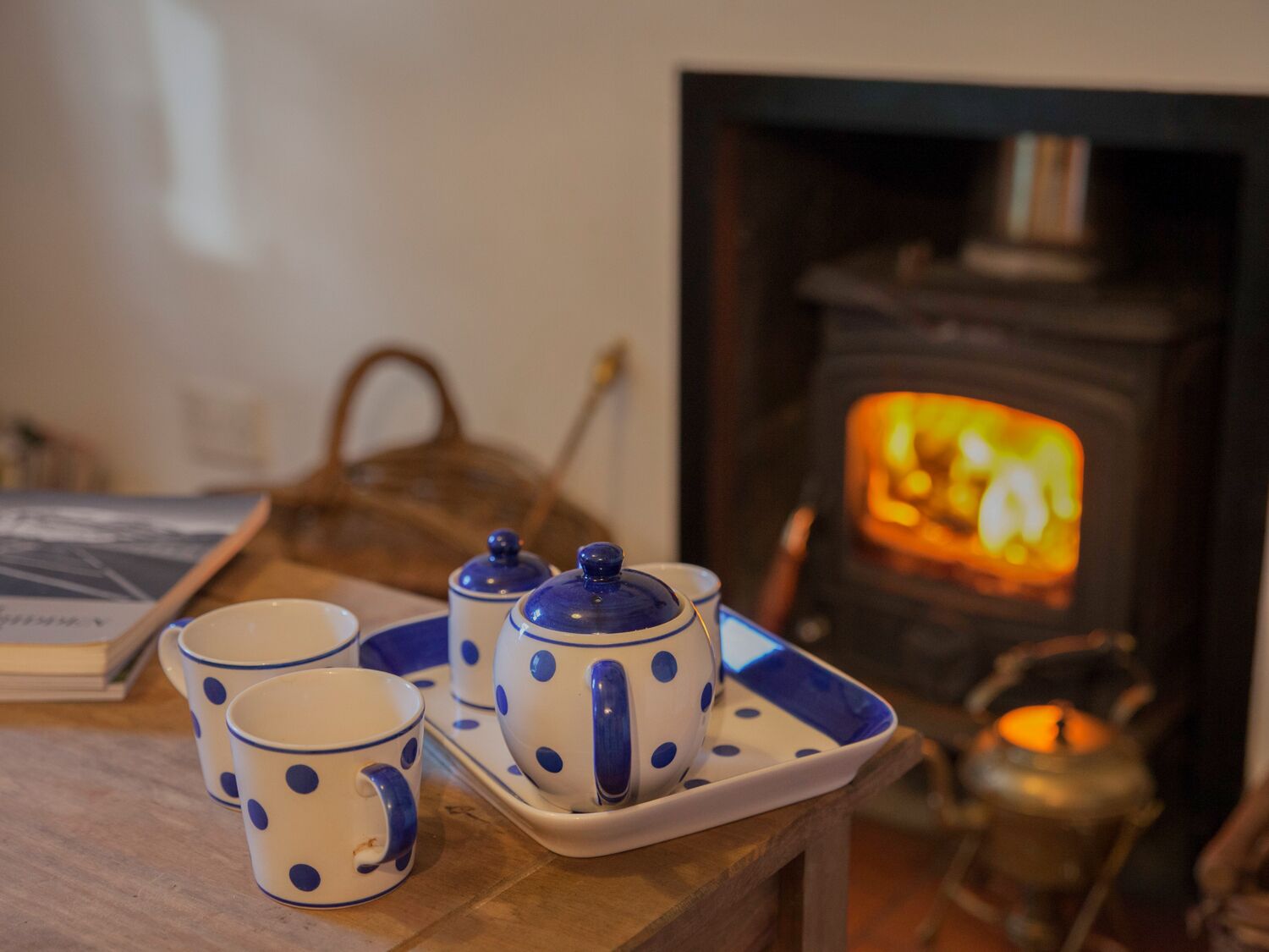 A cozy room with a fireplace, a tray with teacups and a teapot, and a candle on a table.