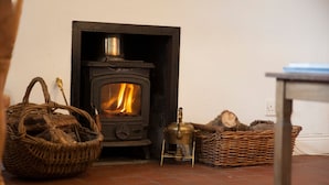 A room with a wood-burning stove, wicker baskets, and a table. - Mr Mcgregors' Cottage (Omagh)
