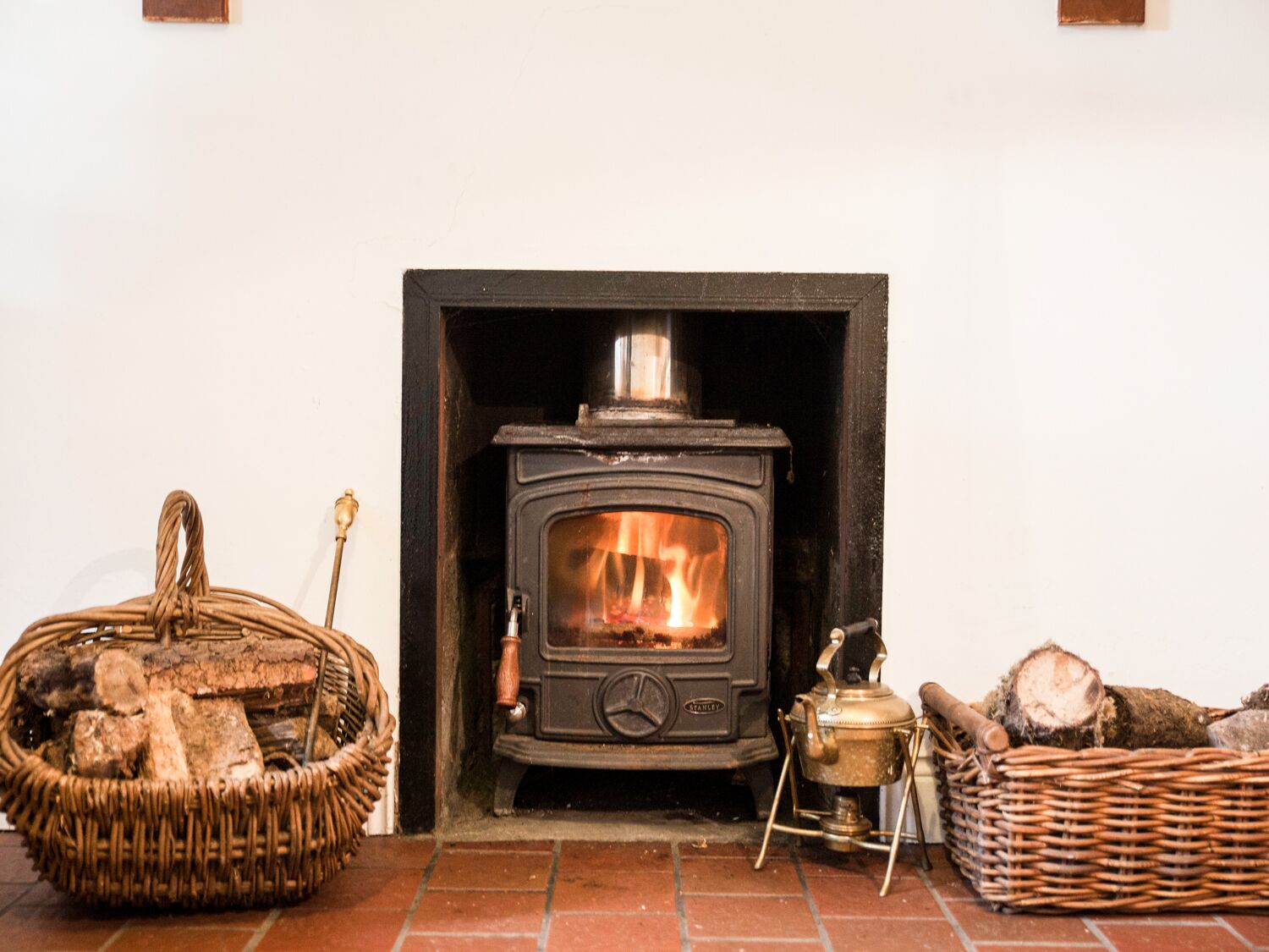 Un poêle à bois installé dans une cheminée, avec du bois de chauffage et un panier à proximité.