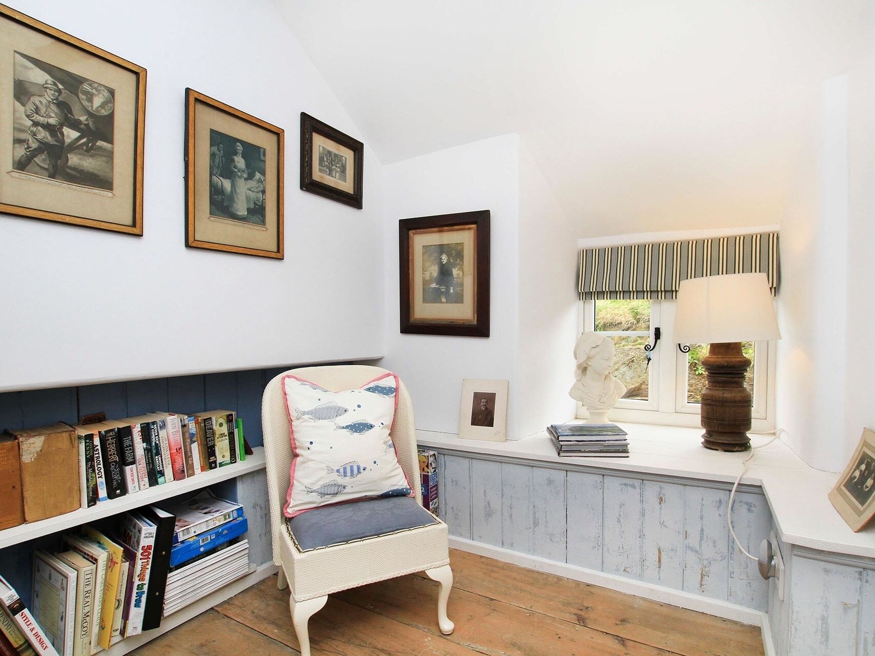 A cozy reading nook with a wicker chair, a bookshelf filled with books, and framed pictures on the wall.