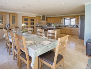 A spacious kitchen with wooden cabinets, a dining area with a table set for four, and a large island with a sink. - Dol Fraint (Gaerwen)