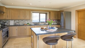 Une cuisine moderne avec des meubles en bois, un îlot central doté de tabourets de bar, un four encastré et une fenêtre avec des stores.