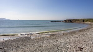 A pebble beach with calm waters and a distant view of a ship. - Stabl Bach (Holyhead)