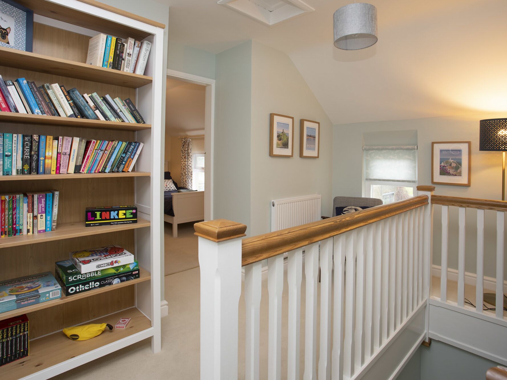 Una habitación bien iluminada con una escalera de madera, una estantería llena de libros y una cama al fondo.