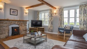A cozy living room with a stone fireplace, a television, a sofa, and a coffee table. - Stabl Bach (Holyhead)
