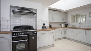 A modern kitchen with white cabinets, a black stove, and a wooden countertop. - Stabl Bach (Holyhead)