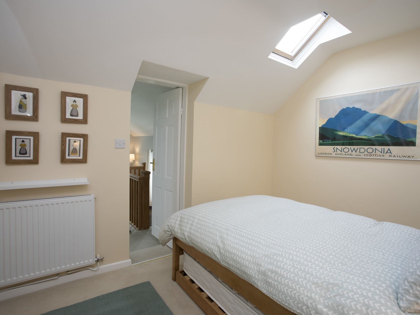 Une chambre avec un lit, un radiateur, une lucarne et une affiche accrochée au mur.