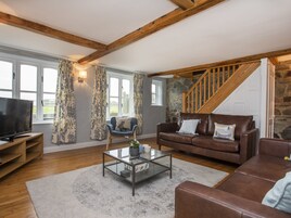 Una sala de estar acogedora con una escalera de piedra, vigas de madera, un televisor, un sillón azul y un sofá de cuero marrón.