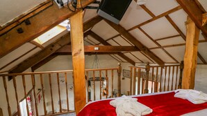 A bedroom with a red bedspread, wooden beams, a television mounted on the ceiling, and a view of the outdoors through a window. - The Mill (Llandysul)