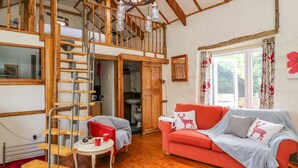 A spacious loft-style room with a wooden staircase, a red sofa, and a red rug. - The Mill (Llandysul)