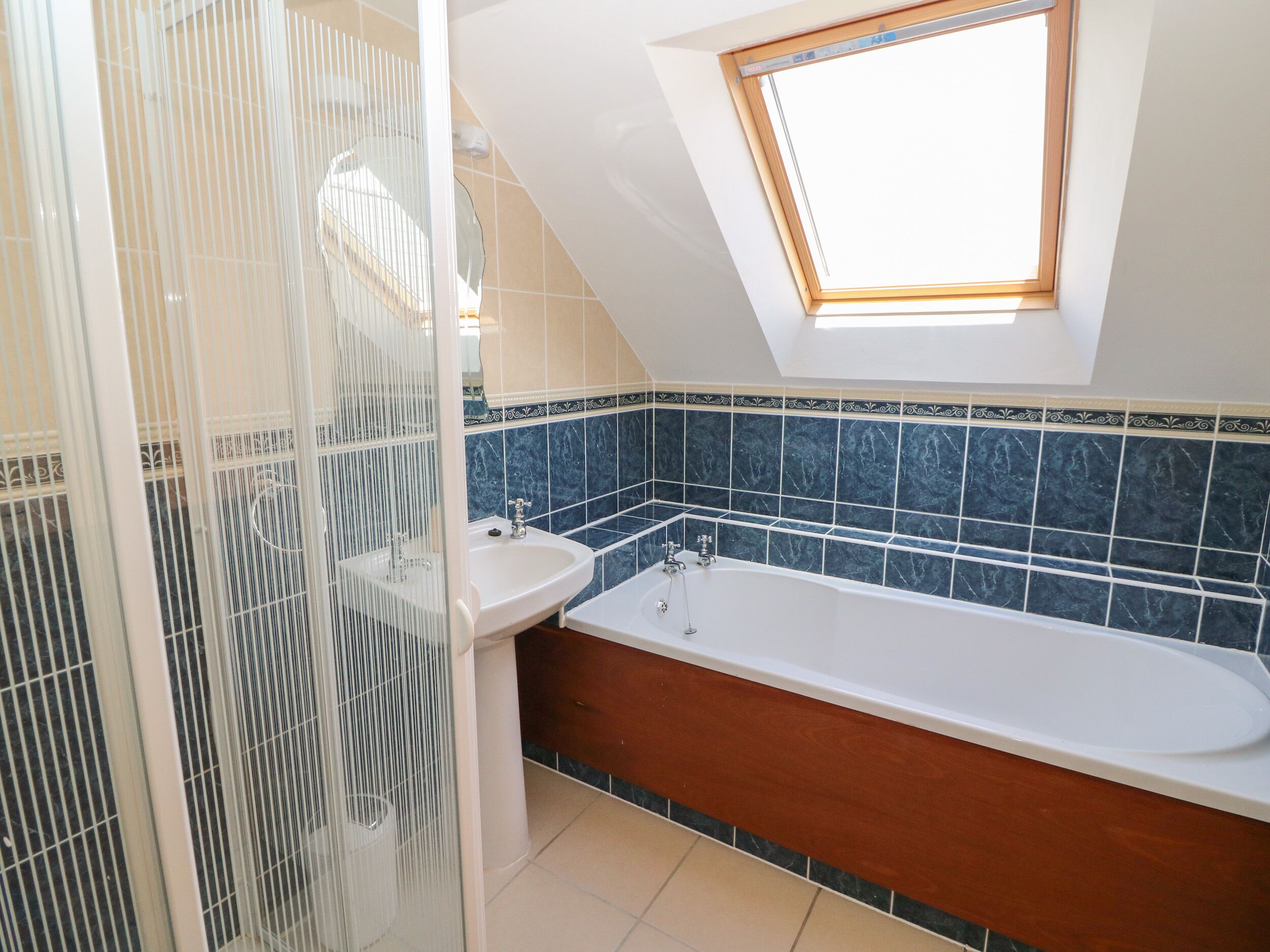 A bathroom with a skylight, a bathtub, a sink, and a shower enclosure.