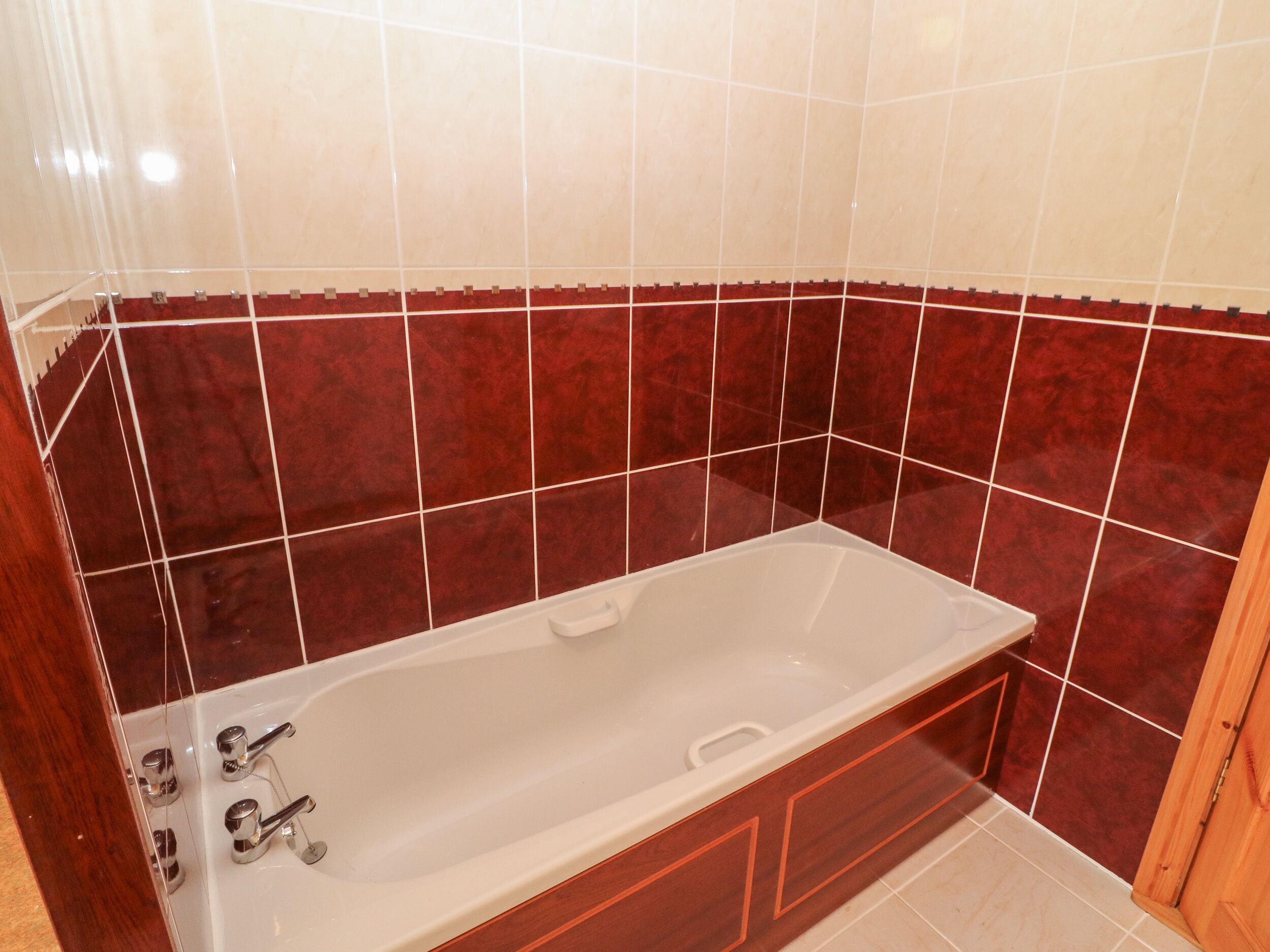 Un baño con bañera, baldosas blancas y rojas, y muebles de madera.