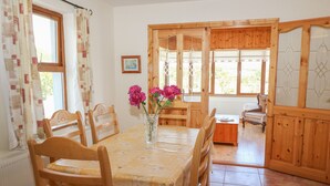 Un comedor con una mesa y sillas de madera, un jarrón con flores y vistas a través de una puerta de madera.