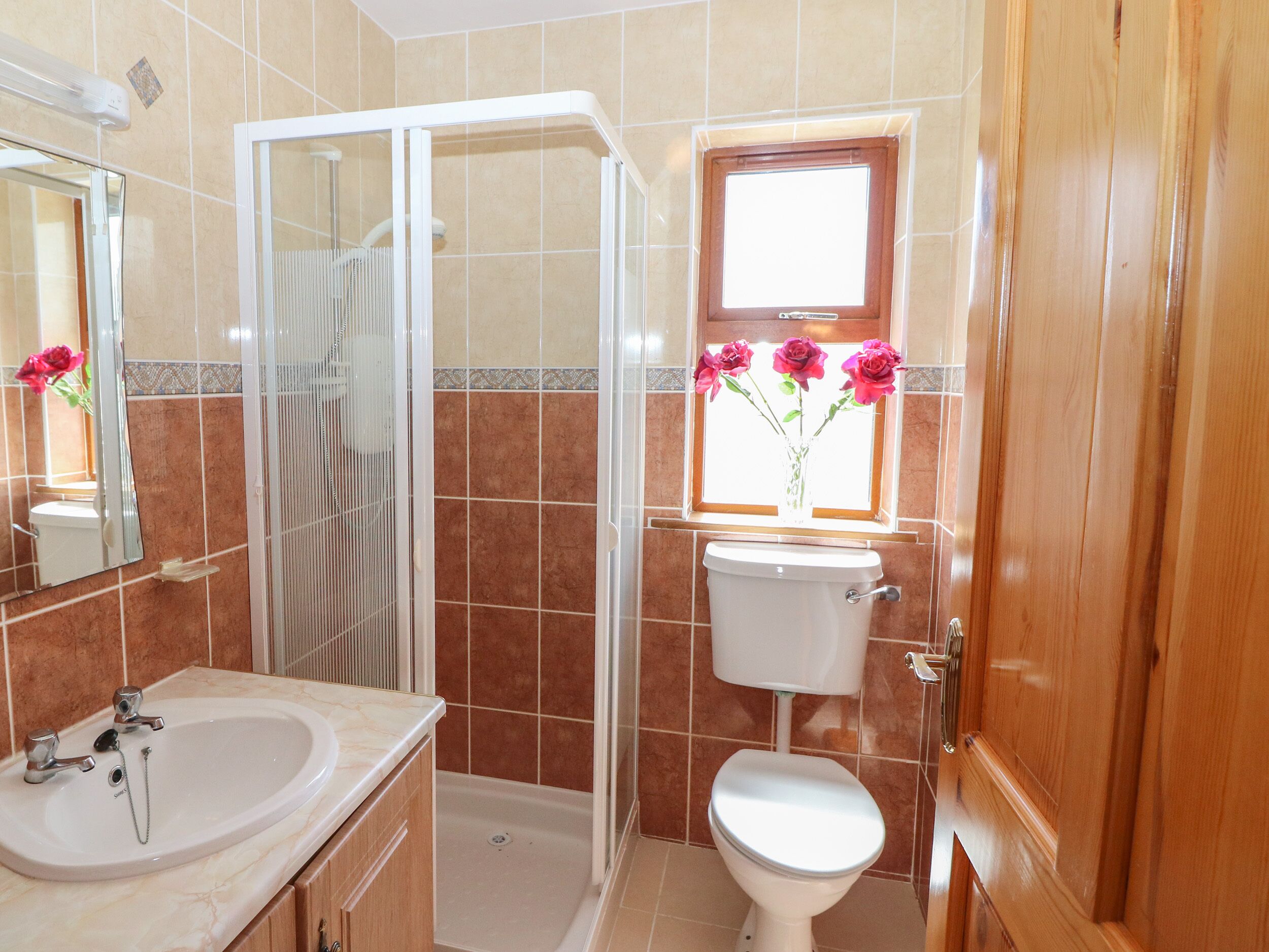 A bathroom with a shower, toilet, sink, and a window with flowers.