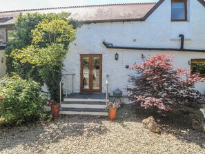 A white building with a wooden door, steps leading to the entrance, and potted plants.