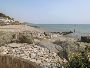 A rocky beach with a wooden fence and houses in the background. - Stable Cottage, Narberth (Narberth)