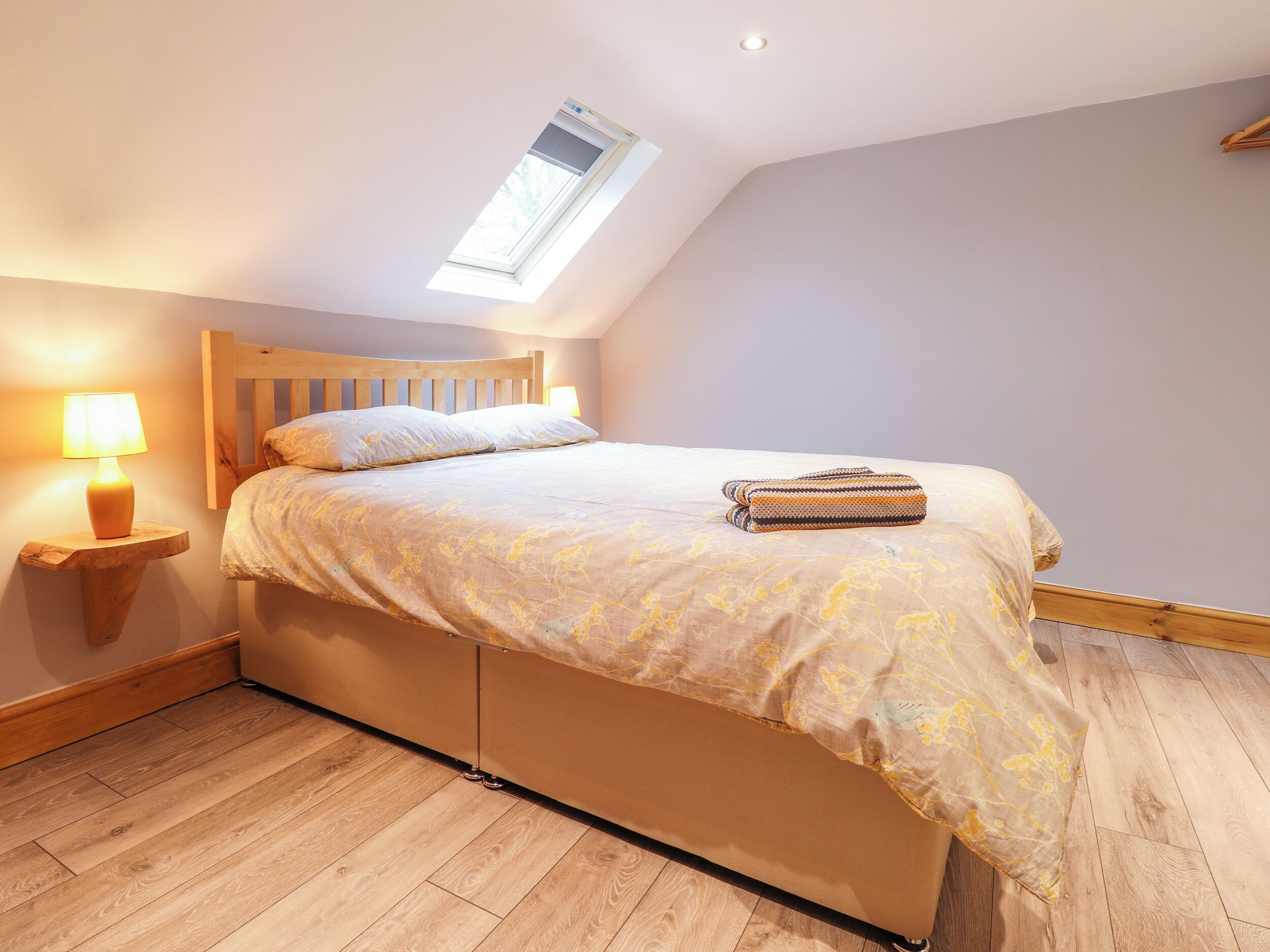 Ein Schlafzimmer mit einem Holzbett, einem Nachttisch mit Lampe, einem Oberlicht und Holzböden.