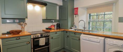 A kitchen with green cabinets, a double oven, a dishwasher, and a window with a view of trees.