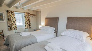 Ein Hotelzimmer mit zwei Betten, jeweils mit Kopfteil, einem Fenster mit Vorhängen, einem Nachttisch und einer Lampe.