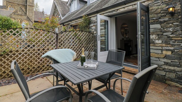 An outdoor patio with a table and chairs, a bottle of champagne, and a stone wall. - The Sanctuary (Windermere)