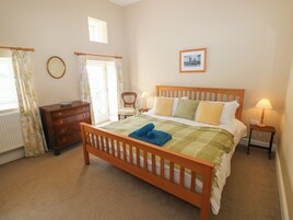 Un dormitorio con una cama de madera, una mesita de noche, un aparador, una silla y una ventana con cortinas.