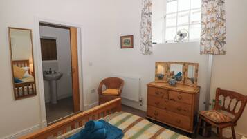 Quarto com cama, cômoda, cadeira, janela com cortinas, espelho e porta que dá para um banheiro.