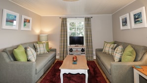 A living room with two grey sofas, a wooden coffee table, a red rug, a television, and a window with curtains. - Craggan Cottage - Balmacara (Kyle)
