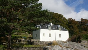 A white house with a stone wall and a large tree in front. - Craggan Cottage - Balmacara (Kyle)