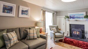 A cozy living room with a sofa, armchair, fireplace, and artwork on the walls. - Craggan Cottage - Balmacara (Kyle)
