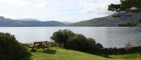 A picnic table on a grassy area with a lake and mountains in the background.