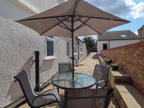 A patio with a glass table and chairs, an umbrella, and a brick wall.