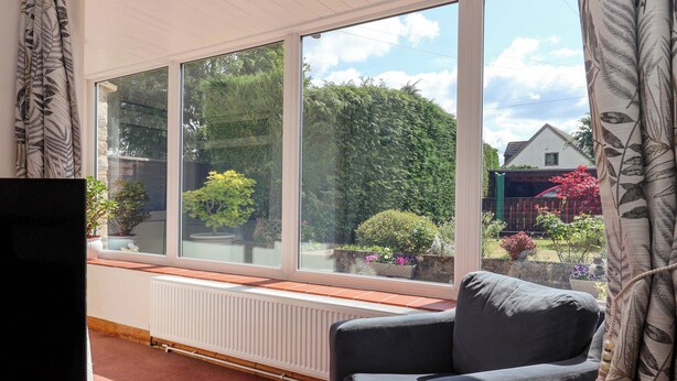 A room with a large window, a radiator, a grey armchair, and a television. - 3 Springhaven (Godalming)
