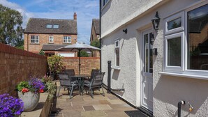 A patio with a table and chairs, a potted plant, and a white building with a window and door. - 3 Springhaven (Godalming)