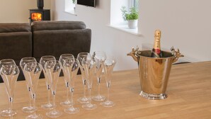A room with a wooden table, a sofa, a TV, a fireplace, and a bottle of champagne in a decorative holder. - Black Lion Barn Retreat (Shrewsbury)