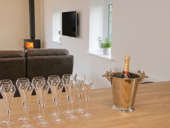 A room with a wooden table holding a champagne bottle and glasses, a sofa, a TV, and a fireplace.