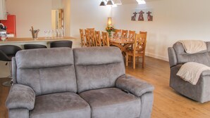 A modern living room with a grey sofa, wooden dining table, and chairs. - Black Lion Barn Retreat (Shrewsbury)