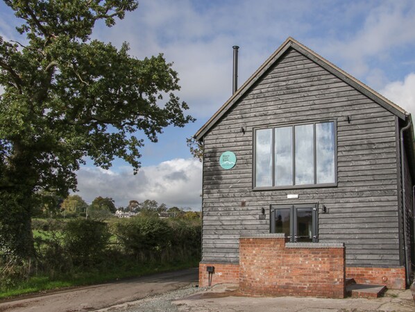 A rustic wooden building with a brick foundation, a large window, and a chimney. - Black Lion Barn Retreat (Shrewsbury)