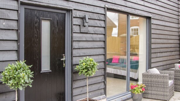 A dark wooden house with a black door, a sliding glass door, and two potted plants. - Black Lion Barn Retreat (Shrewsbury)