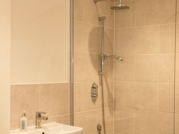 A bathroom with a shower, sink, and a bottle of soap.