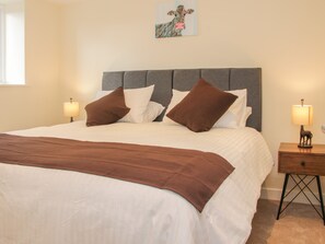 A neatly made bed with a brown blanket and pillows, a grey upholstered headboard, and two bedside tables with lamps. - Black Lion Barn Retreat (Shrewsbury)