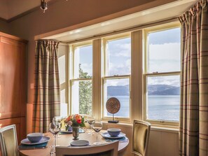 Un comedor con una mesa dispuesta para cuatro, ventanas amplias con cortinas y vistas a un cuerpo de agua y montañas.