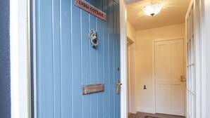 Una porta blu con una targa che recita "LYDIA COTTAGE" e un citofono. Si intravede un corridoio con un tappeto e una porta che dà su una stanza.