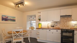 Una cucina con mobili bianchi, un piano cottura nero e un'area pranzo con tavolo in legno e sedie bianche.