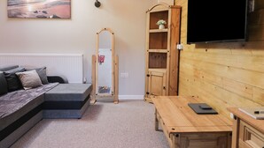 A cozy room with a sofa, a wooden table, a TV, and a mirror. - Dovecote Cottage (Scarborough)