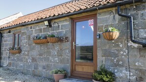 A stone building with a tiled roof, a wooden door, and three hanging flower baskets. - Dovecote Cottage (Scarborough)