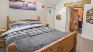 A bedroom with a wooden bed, a skylight, a painting of a sunset, a fire exit sign, and a stone wall. - Dovecote Cottage (Scarborough)
