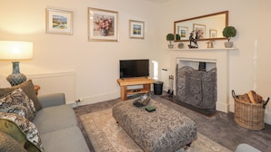Ein Wohnzimmer mit einer Couch, Hocker, Kamin, Fernseher und gerahmten Bildern an der Wand.